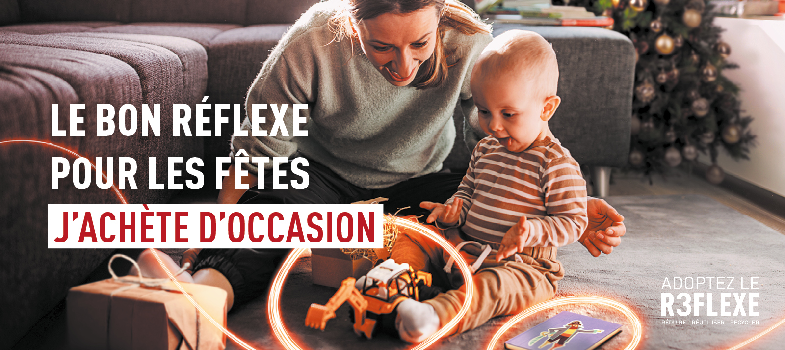 Scène familiale de fêtes montrant un adulte et un jeune enfant jouant ensemble avec des jouets d’occasion près d’un sapin décoré, accompagnée du message “Le bon réflexe pour les fêtes : j’achète d’occasion” et du slogan “Adoptez le R3flexe – réduire, réutiliser, recycler”.